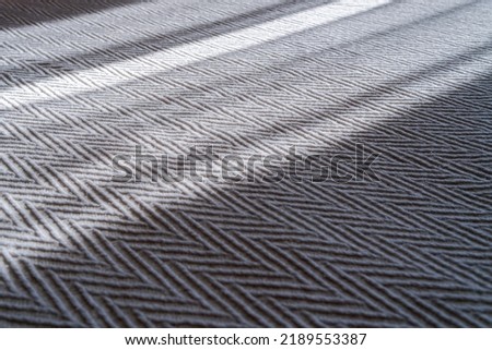 A close up view of a bedspread with a clearly visible fabric texture and weave. The sun's rays through the window fall on the bedspread. Zigzag or chevron pattern.