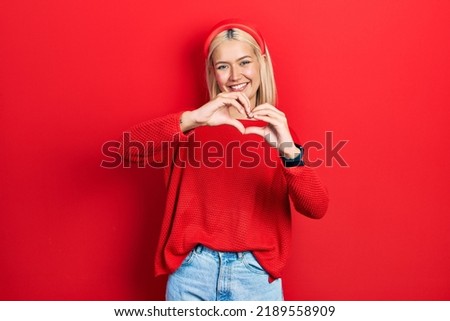 Beautiful blonde woman wearing casual red sweater smiling in love doing heart symbol shape with hands. romantic concept. 