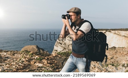 traveler taking wonderful photos of cliffs with travel photography backpack. Travel photographer with eye on photo camera viewfinder shooting landscape over sea. panoramic travel photography