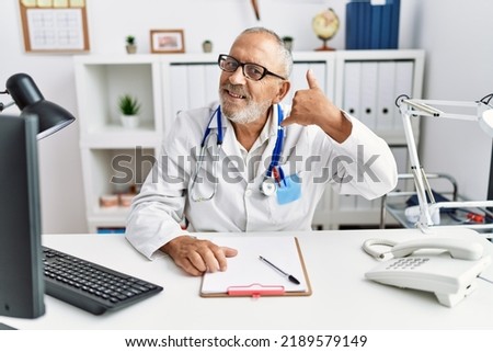Mature doctor man at the clinic smiling doing phone gesture with hand and fingers like talking on the telephone. communicating concepts. 