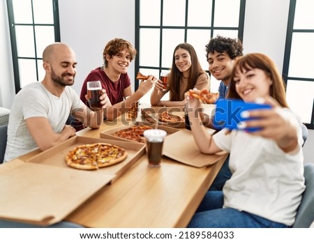 Group of young friends smiling happy eating italian pizza making selfie by the smartphone at home.