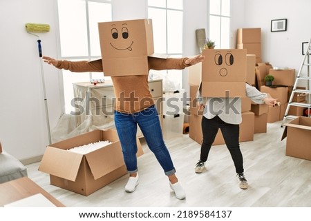 Mature mother and down syndrome daughter moving to a new home, standing wearing cardboard boxes with funny faces over head