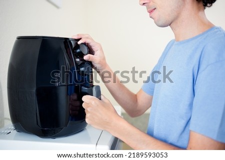 close up of an air fryer while one hand holds the food container and the other hand adjusts the time and temperature on the regulation knob. Royalty-Free Stock Photo #2189593053