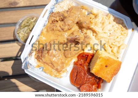 A top down view of a styrofoam container of soul food, featuring smothered chicken.