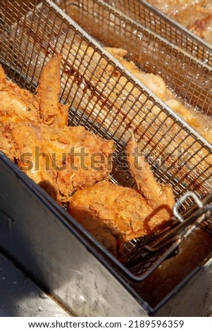 A view looking into a deep fryer machine full of fried chicken pieces.
