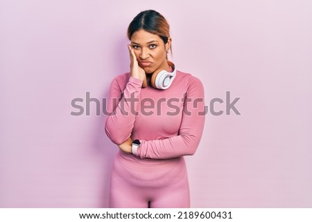 Beautiful hispanic woman wearing gym clothes and using headphones thinking looking tired and bored with depression problems with crossed arms. 