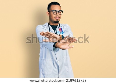 Young african american man wearing doctor uniform and stethoscope rejection expression crossing arms and palms doing negative sign, angry face 