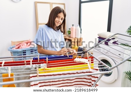 Young hispanic girl hanging laundry on cloth line at laundry room