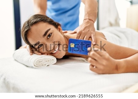 Latin man and woman wearing physiotherapy uniform having back massage holding credit card at beauty center