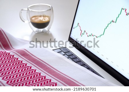 Focus on laptop screen with charts, coffee, and Saudi scarf, headdress Royalty-Free Stock Photo #2189630701