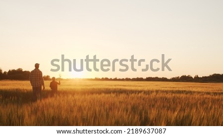 Farmer and his son in front of a sunset agricultural landscape. Man and a boy in a countryside field. Fatherhood, country life, farming and country lifestyle. Royalty-Free Stock Photo #2189637087