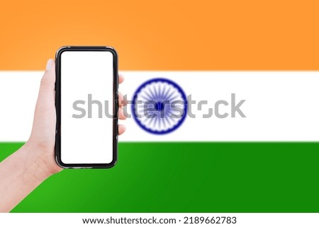Close-up of male hand holding smartphone with blank on screen, on background of blurred flag of India.