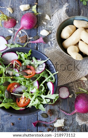 rocket salad on bowl with radish and tomatoes slices and seed with bread sticks on rustic table with whole radish