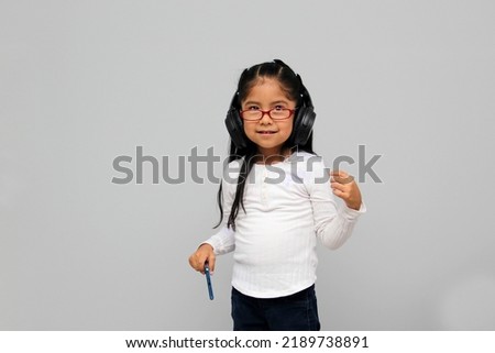 4-year-old brunette Latin girl with glasses listens to music in her headphones connected to her cell phone dances, sings and enjoys the rhythm happy and excited
