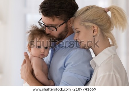 Close up affectionate young parents spend time together with newborn baby, dad holds on arms kissing infant feeling unconditional love, enjoy tender moments. Happy parenthood, family, adoption Royalty-Free Stock Photo #2189741669