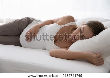 Close up pregnant woman in comfort nightwear sleeps in bed, looking peaceful, touch her big belly enjoy healthy daytime nap, take break in bedroom on fresh white sheets. Late pregnancy, rest concept Royalty-Free Stock Photo #2189741745