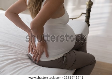Unknown pregnant woman feels pain in muscles, joints of lower back, touch back to relieve ache, close up, rear view. Strain on vertebrae due to late pregnancy, kidney problem, third trimester Royalty-Free Stock Photo #2189741749