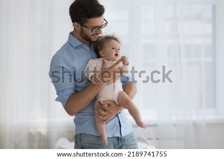 Young father holding on hands new-born baby. Loving daddy in glasses standing indoor spend priceless time together with infant. Happy Fathers Day, fatherhood, family ties, unconditional love concept Royalty-Free Stock Photo #2189741755