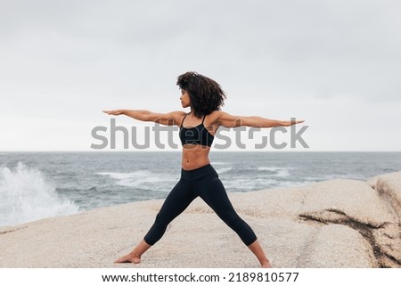 Side view of yong woman performing warrior pose against ocean Royalty-Free Stock Photo #2189810577