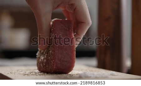 man rubbing raw beef steak with spices on oak board closeup, wide photo