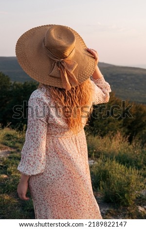 Woman holds hat in her hand and looks at nature in sunset light. Selective focus. Picture for articles about women, success, psychology.