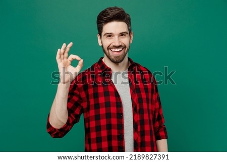 Young happy smiling satisfied cheerful fun caucasian man he 20s wearing red shirt grey t-shirt showing okay ok gesture isolated on plain dark green background studio portrait People lifestyle concept