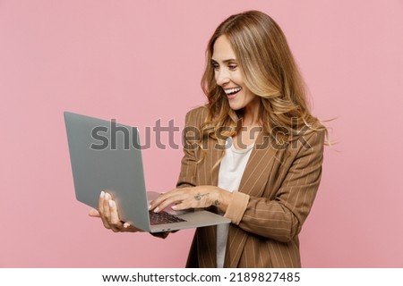 Young smiling happy fun cheerful successful employee business woman 30s she wear casual brown classic jacket hold use work on laptop pc computer isolated on plain pastel light pink background studio