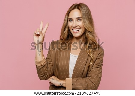 Young cool smiling happy fun friendly cheerful successful employee business woman 30s she wearing casual brown classic jacket showing victory sign isolated on plain pastel light pink background studio