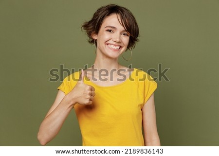 Young smiling satisfied cheerful fun cool happy woman she 20s wear yellow t-shirt showing thumb up like gesture isolated on plain olive green khaki background studio portrait. People lifestyle concept Royalty-Free Stock Photo #2189836143