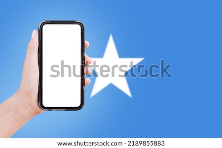 Close-up of male hand holding smartphone with blank on screen, on background of blurred flag of Somalia.