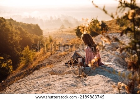 Beautiful child girl on the mountain peak with dry yellow grass reading a book, at beautiful mountains in fog at sunrise in autumn. Colorful landscape. Travel and tourism
