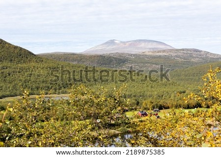 A wide landscape of Finnish Lapland from road no. 970. The Teno river flows in the foreground of the picture. On the other side of the river is a red wooden house and a high fell.