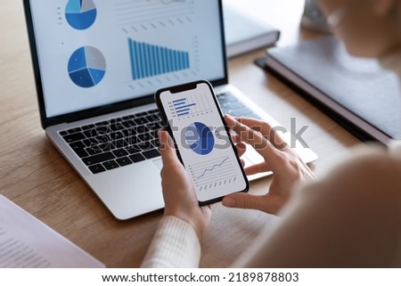 Close up over the shoulder view of female employee work on computer and smartphone analyze financial statistics in office. Woman worker busy brainstorm consider finances, using laptop and cellphone. Royalty-Free Stock Photo #2189878803
