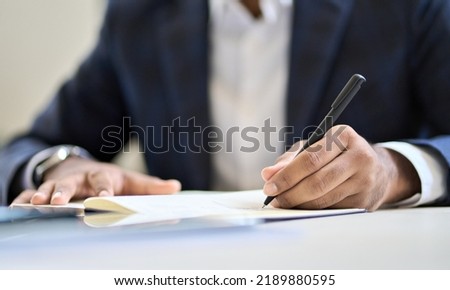Business man lawyer executive wearing suit holding pen in hand writing in notebook or contract legal financial document, filling insurance form, taking notes, putting signature in corporate papers. Royalty-Free Stock Photo #2189880595