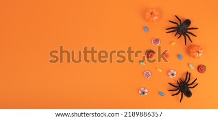 Halloween sweets and horrible spiders on orange background. Halloween concept, top view, copy space