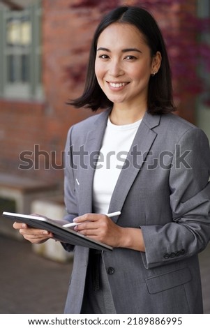 Smiling young adult elegant professional leader Asian business woman, chinese female hr or marketing manager, korean businesswoman wearing suit holding tablet looking at camera, vertical portrait. Royalty-Free Stock Photo #2189886995