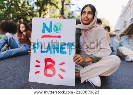 Muslim girl holding a "No planet B" poster at a climate change demonstration. Group of multicultural youth activists protesting against global warming. Young people joining the global climate strike.