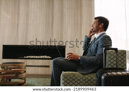 Side view of smiling businessman with laptop talking on cellphone at the airport waiting lounge. Business traveler in airport lounge waiting for flight. Royalty-Free Stock Photo #2189909463