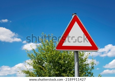 Blank red european warning traffic sign triangle in front of cloudy sky in summer