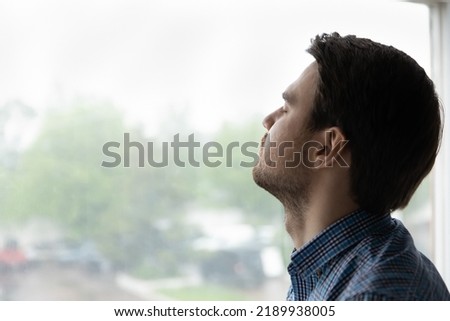 Close up of young 35s man closed his eyes pose on window background, guy take break, relieving fatigue or stress makes breath exercises, enjoy fresh conditioned air and climate control inside Royalty-Free Stock Photo #2189938005