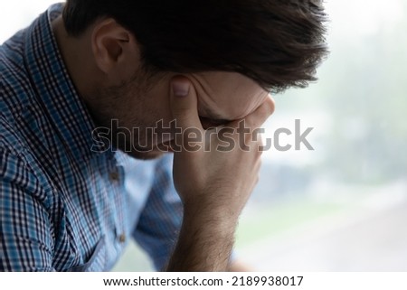 Sad hopeless young man sit alone indoor looks desperate, cover face with head suffers, troubled with concerns, divorce or drama feeling unhappy after quarrel or breakup, psychological problem Royalty-Free Stock Photo #2189938017