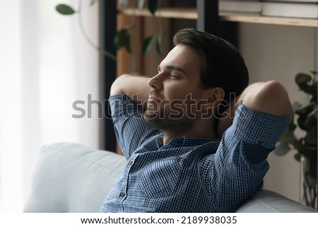 Climate control, air conditioning system inside for comfort life and rest concept. Young serene man closed eyes put hands behind head relax leaned on sofa daydreams enjoy day off at modern cozy Royalty-Free Stock Photo #2189938035