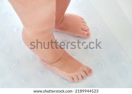 Toddler baby legs is standing on a non-slip mat in the bathtub. Child boy foots washes on the anti slip carpet in the bathroom. Kid age one year Royalty-Free Stock Photo #2189944523