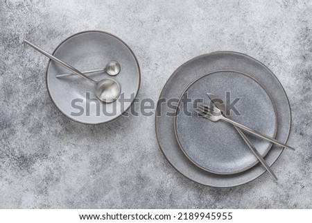 Gray ceramic plates and cutlery on a gray stone background. Modern craft crockery for table setting. Top view. Royalty-Free Stock Photo #2189945955