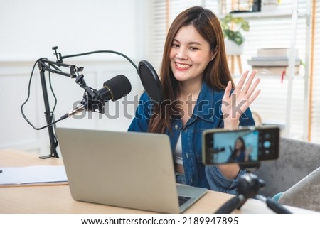 Asian woman use microphone wear headphone record content with smart phone for online audience listen at home.Social media influencer recording online broadcast.