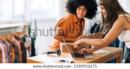 Clothing store owners having a discussion while preparing online orders for shipping. Two young women using a laptop together in a thrift store. Female entrepreneurs running an e-commerce business Royalty-Free Stock Photo #2189952675