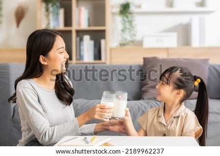 Asian mother and her daughter clink glasses enjoy and smile with milk drink.Mom and little girl holding milk glasses and drink to get calcium.Healthy Eating Concept Royalty-Free Stock Photo #2189962237
