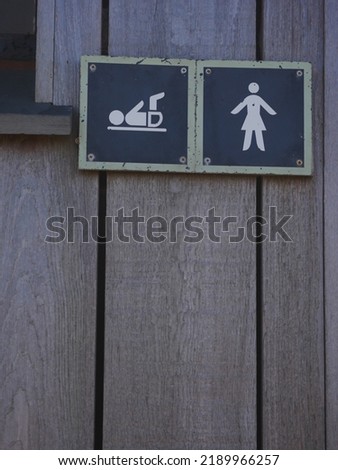 Icons for female washroom and baby change facilities on wooden door of public toilets