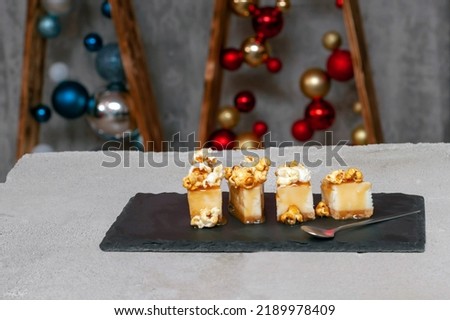cheesecake with salted caramel and popcorn on a black slate board with a spoon in the middle of the photo, with Christmas balls in the background.