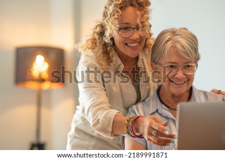 Beautiful mature blonde woman teaching her mother how to use laptop browsing on internet Royalty-Free Stock Photo #2189991871
